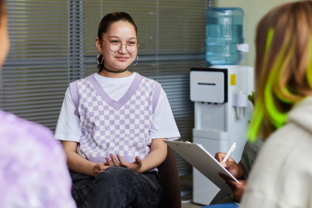 Teen smiling in group session with clinician holding clipboard